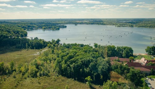 Aerial view of a serene lake surrounded by lush greenery and trees under a partly cloudy sky.