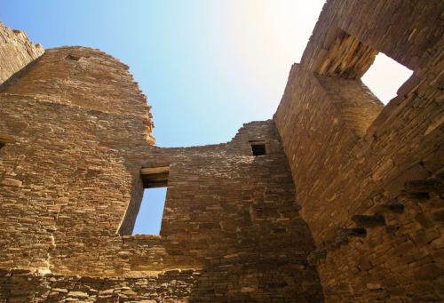 Ruins of an ancient stone structure under a clear blue sky, showcasing weathered walls and open windows.