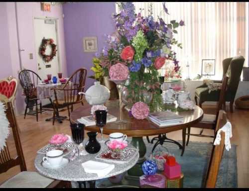 A cozy tea room with a floral centerpiece, elegant table settings, and colorful decor in a pastel-colored space.