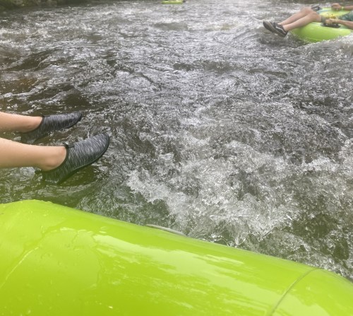 Two pairs of feet in water, resting on bright green inner tubes, with rippling water visible around them.