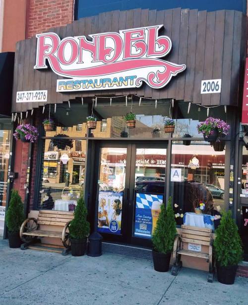 Front view of Rondel Restaurant, featuring a wooden sign, flower pots, and outdoor seating.
