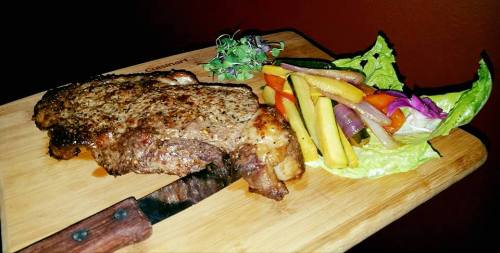 A juicy steak on a wooden cutting board, accompanied by a colorful assortment of grilled vegetables and fresh greens.