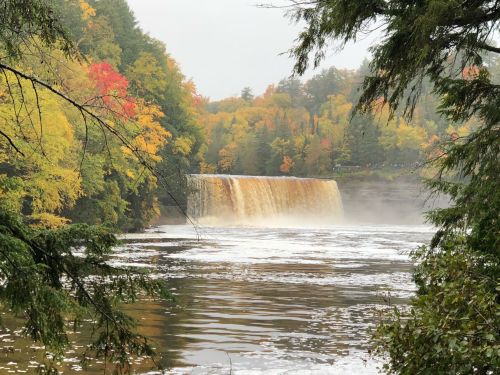 A scenic view of a waterfall surrounded by colorful autumn foliage and a misty river.