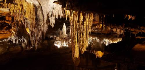 Stalactites and stalagmites illuminated in a dark cave, showcasing intricate rock formations.