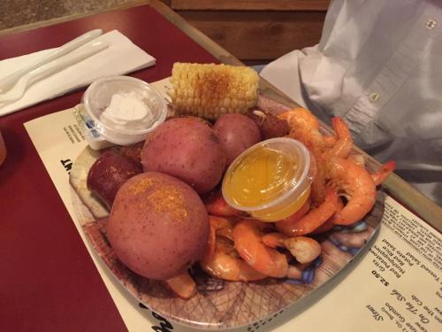 A plate of shrimp, red potatoes, corn on the cob, and dipping sauces, served on a restaurant table.