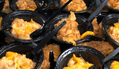 Close-up of individual servings of cheesy casserole in black cups, each with a plastic spoon.