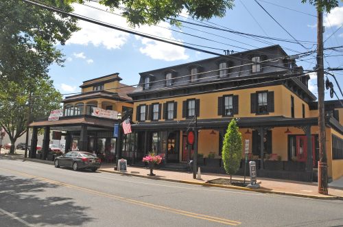 A charming yellow and black building with an American flag, surrounded by trees and parked cars on a sunny day.