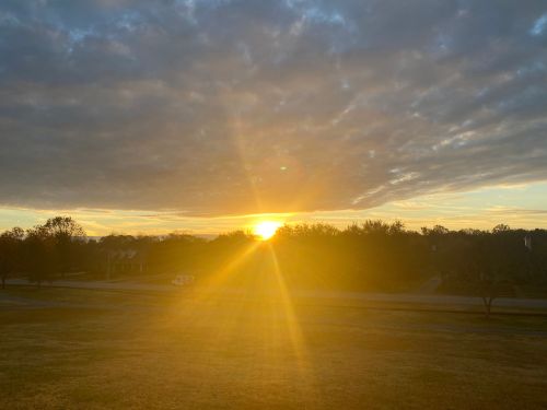 A sunrise over a landscape, with golden light breaking through clouds and illuminating the horizon.