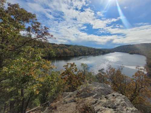 A scenic view of a river surrounded by trees under a partly cloudy sky, with sunlight reflecting on the water.