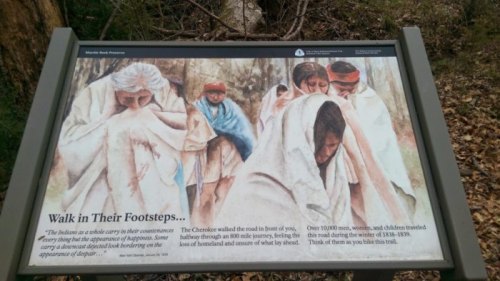 Sign depicting a historical narrative about the Trail of Tears, featuring figures in blankets, reflecting sorrow and hardship.