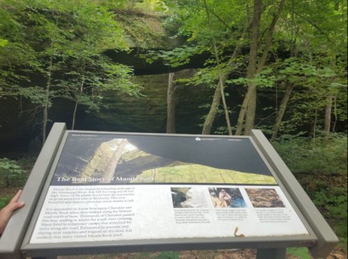 A sign in a forest explaining the history of Mound Rock, surrounded by lush greenery and rock formations.
