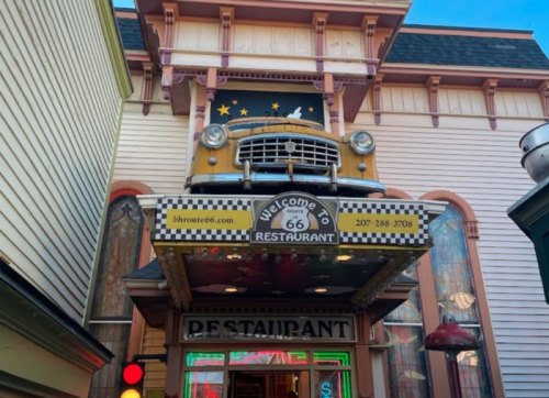 A vintage yellow car is mounted above the entrance of a Route 66-themed restaurant with colorful signage.