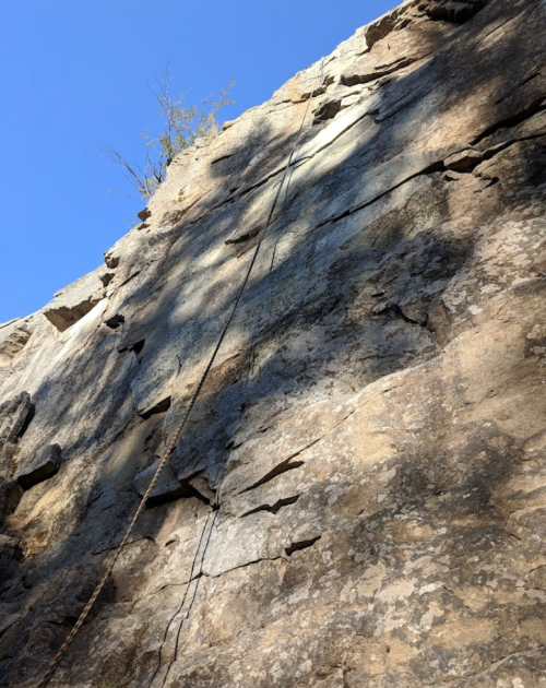 A steep rock face with a climbing rope hanging down, under a clear blue sky.