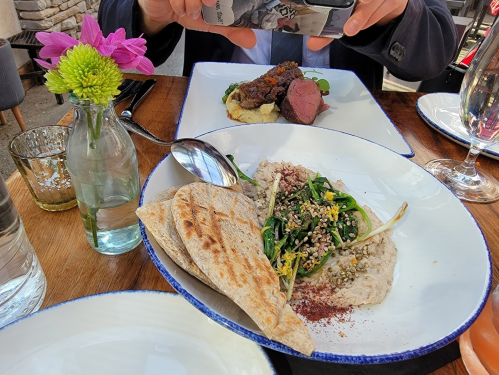 A table setting with a bowl of salad, flatbread, and a person taking a photo of a plated dish in the background.