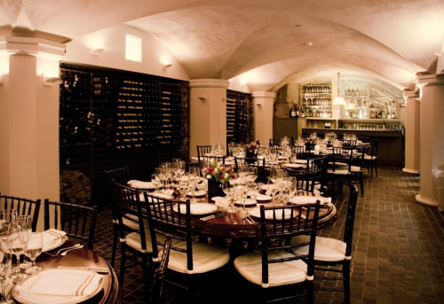 Elegant restaurant interior with round tables, wine racks, and a bar, featuring soft lighting and a cozy atmosphere.