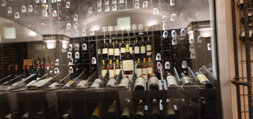 A wine cellar displaying various bottles on shelves, with labels visible through a glass enclosure.