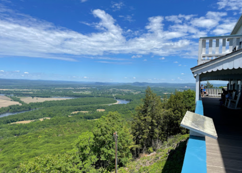 A scenic view from a balcony overlooking lush green hills and a winding river under a bright blue sky.