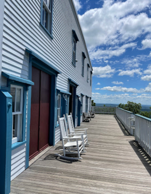 A wooden deck with rocking chairs, overlooking a scenic view under a partly cloudy sky.