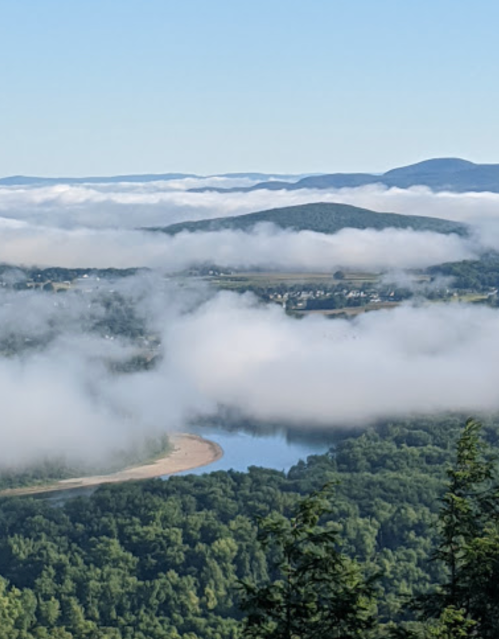 A scenic view of a river winding through lush green hills, surrounded by clouds and a clear blue sky.