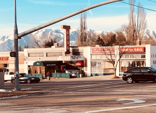 A street view of shops with mountains in the background, featuring a pizza place and a BBQ restaurant.