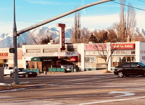 A street view of shops with mountains in the background, featuring a pizza place and a BBQ restaurant.