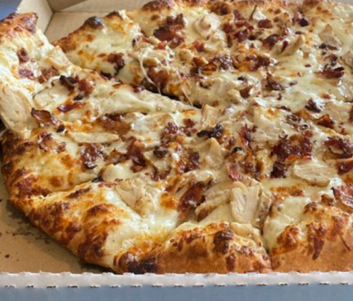 A close-up of a pizza with melted cheese, chicken, and bacon, partially removed from its cardboard box.