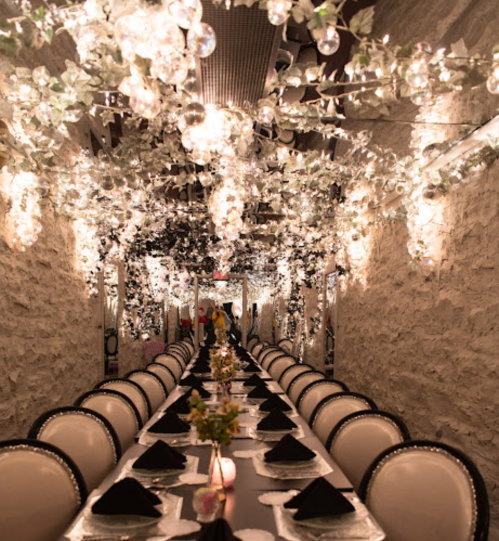 A beautifully decorated dining room with a long table, surrounded by sparkling lights and floral accents.
