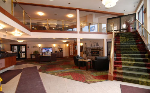 Interior of a hotel lobby featuring a staircase, seating area, and reception desk with warm lighting and decorative elements.