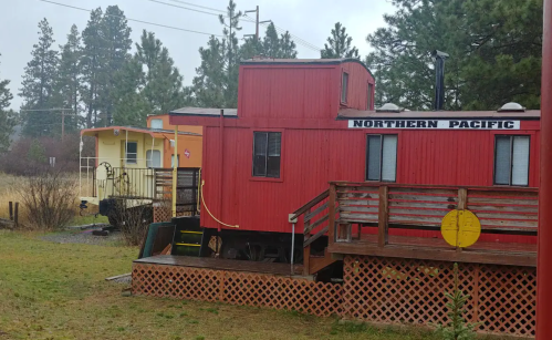 Two colorful train cars, one red labeled "Northern Pacific" and one yellow, set in a grassy area with trees in the background.