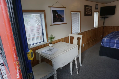 Cozy interior of a small room featuring a table, chair, bed, and framed artwork on the walls.
