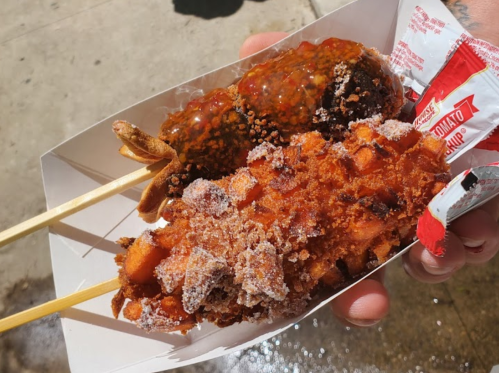 A hand holding a tray with two skewers of deep-fried snacks, one coated in chocolate and the other in cinnamon sugar.