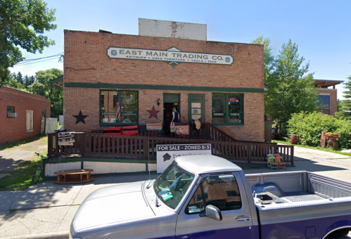 A brick building with "East Main Trading Co." sign, featuring a porch and a pickup truck parked in front.