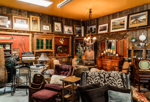 A cozy vintage shop filled with antique furniture, decor, and framed artwork on wooden walls.