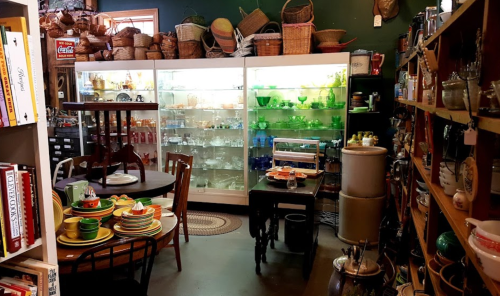 A cozy vintage shop filled with glassware, dishes, and baskets, showcasing a variety of collectibles and home goods.