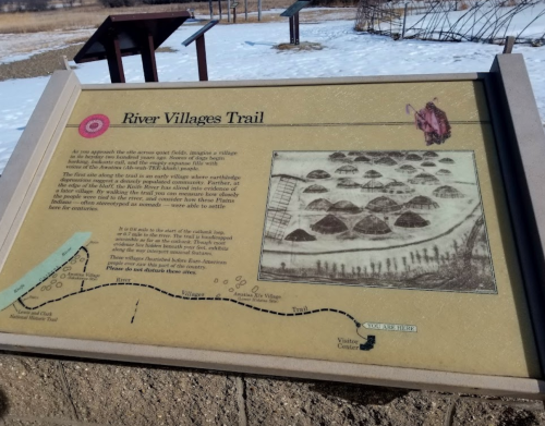 Sign for the River Villages Trail, featuring a historical illustration and a map of the trail's route. Snowy landscape.