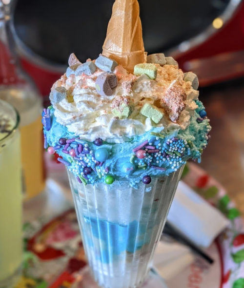 A colorful ice cream sundae topped with whipped cream, sprinkles, and a cone, served in a tall glass.