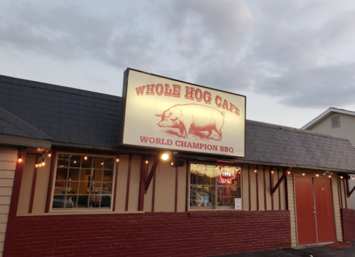 Sign for Whole Hog Cafe, featuring a pig illustration and the text "World Champion BBQ" on a restaurant exterior.