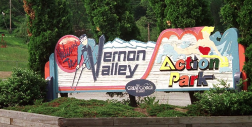 Colorful sign for Vernon Valley Action Park, featuring skiing and amusement park imagery, surrounded by greenery.