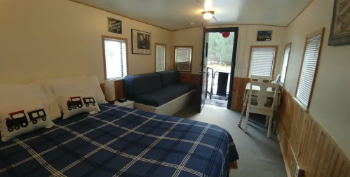 Cozy room with a bed, sofa, and a door leading outside, featuring wooden accents and framed pictures on the walls.