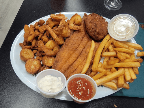 A large platter of fried seafood, including shrimp, fish fillets, hushpuppies, fries, and dipping sauces.