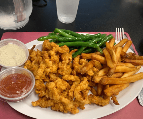 A plate of fried food featuring crispy chicken strips, green beans, and French fries, with dipping sauces on the side.