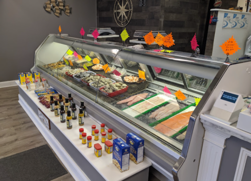 A seafood display case filled with various fish and shellfish, with colorful price tags and condiments in front.
