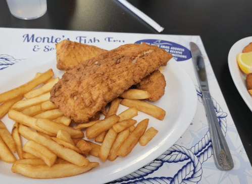 A plate of fried fish fillets served with golden French fries on a restaurant table.