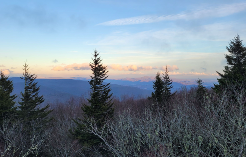 A scenic view of mountains and trees under a pastel sky at sunset, with layers of hills in the background.