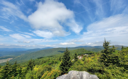 A panoramic view of lush green mountains under a blue sky with scattered clouds.