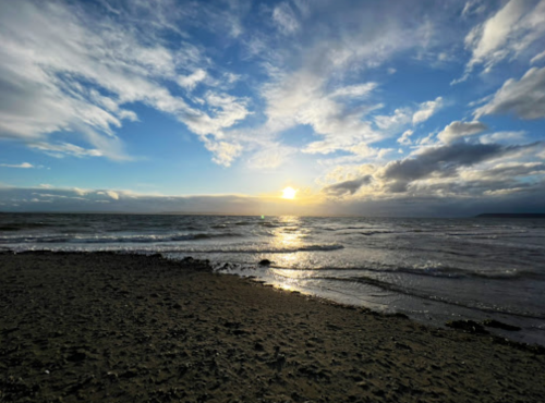 A serene beach scene at sunset, with waves gently lapping the shore under a cloudy sky.