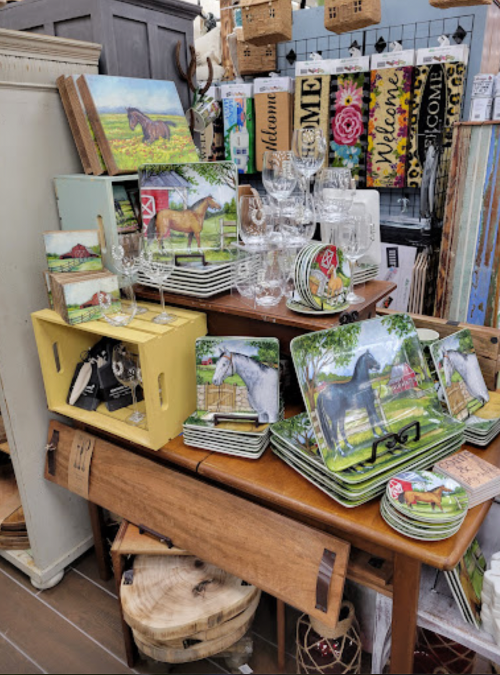 A display of decorative plates and glassware featuring horse-themed designs, arranged on a wooden table.
