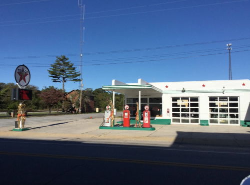 Vintage gas station with red pumps, a Texaco sign, and a clear blue sky in the background.