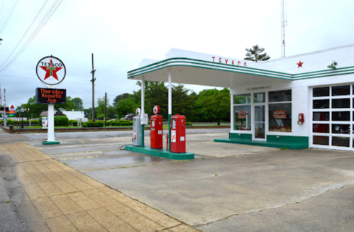 A vintage Texaco gas station with red pumps, green accents, and a cloudy sky in the background.