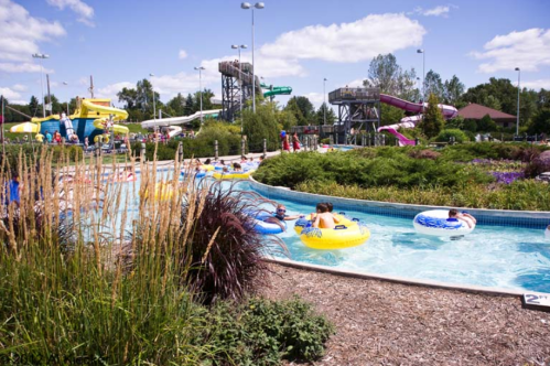 A water park scene with people floating on tubes in a lazy river, surrounded by greenery and water slides in the background.
